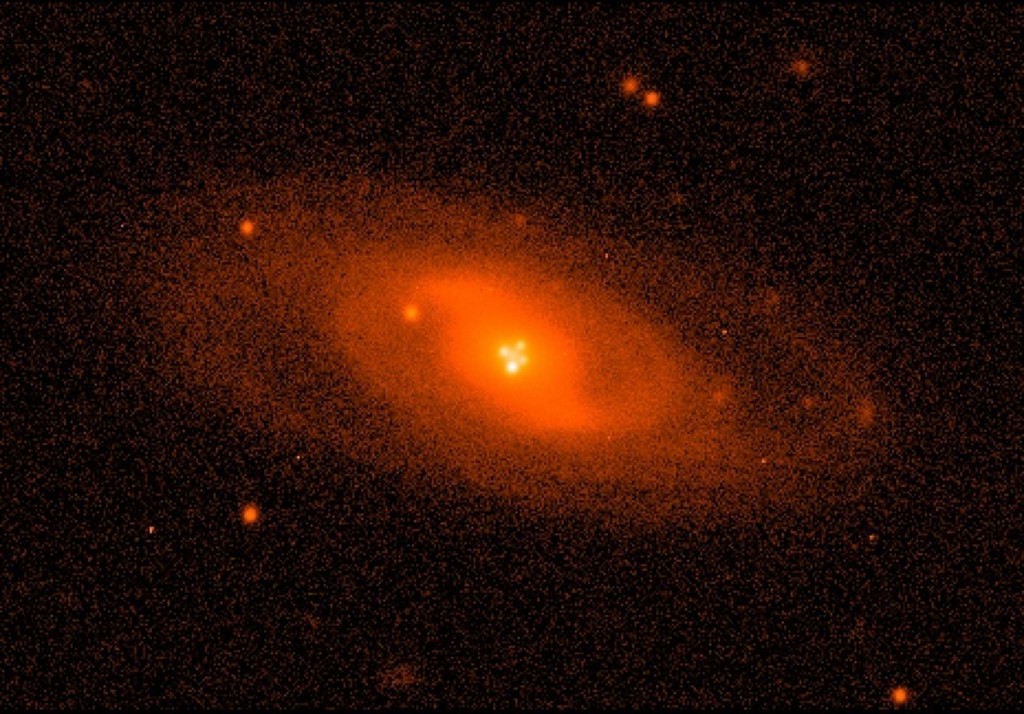 Imagen del sistema lente Q2237+0305 (conocido como La cruz de Einstein) obtenido con el Nordic Optic Telescope. La galaxia espiral hace de lente gravitatoria, y cerca del núcleo pueden verse las cuatro imágenes del cuásar producidas por este efecto. / Mediavilla et al.